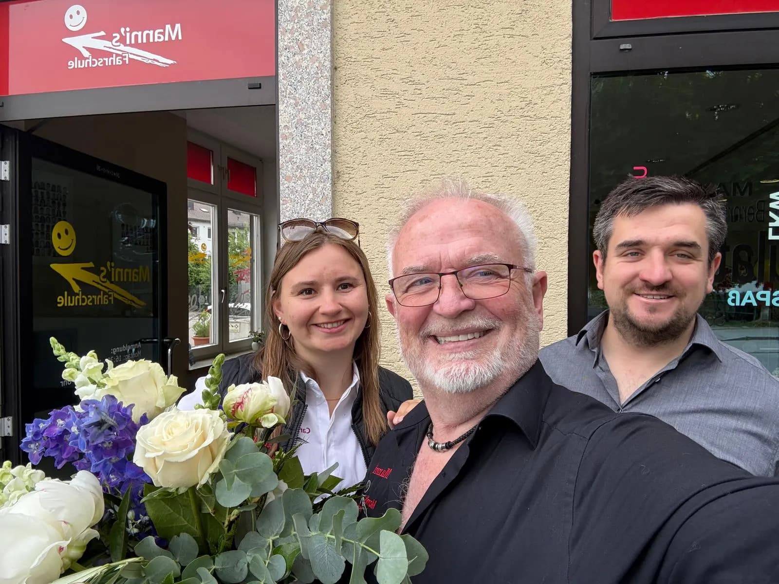 Team-Selfie vor dem Eingang von Manni's Fahrschule mit Blumenstrauß