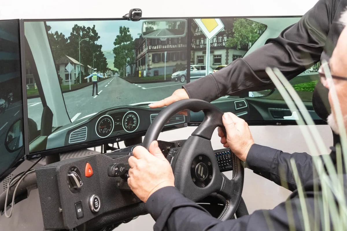 Cockpit-Ansicht des Fahrsimulators mit drei Monitoren bei Manni's Fahrschule — Hände am Lenkrad, realistisches Fahrgefühl